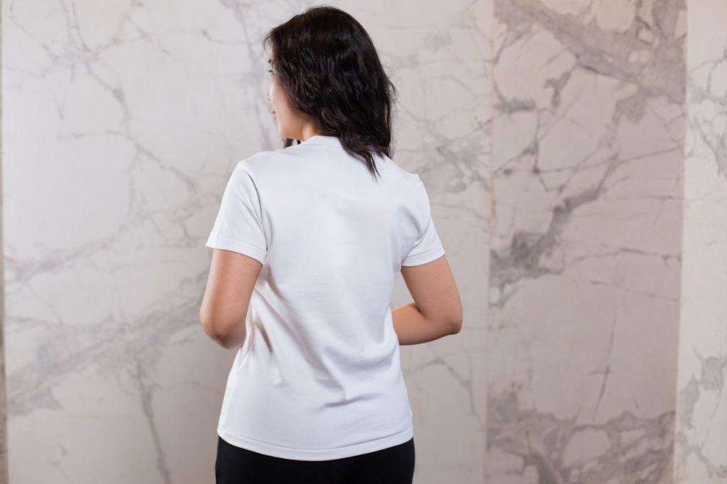 Back view positive female wearing black pant and white t shirt standing against marble wall